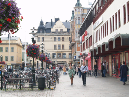 La place principale de Linköping, galerie commerçante Gallerian, des personnes qui se promènent, des bicyclettes dans un parking à vélos, des fleurs dans des jardinières suspendues